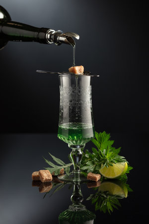 Absinthe is poured from an vintage bottle into a glass. Preparation of the drink. Absinthe with ingredients.の写真素材