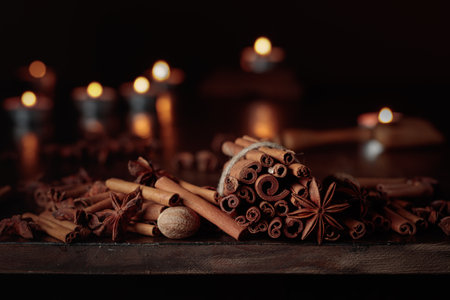 Cinnamon sticks, anise, and nutmeg on an old wooden table. In the background small burning candles.