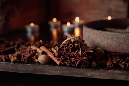 Cinnamon sticks, anise, and nutmeg on an old wooden table. In the background small burning candles.の写真素材