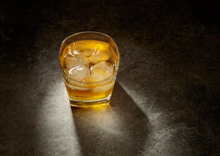 Whiskey in a crystal glass with ice on an old stone table. Hard light with beautiful shadow. Copy space.の写真素材