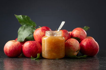 Jar of apple jam and red fresh apples with leaves on a black background.の写真素材