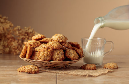 Oatmeal cookies and milk sit on a kitchen table. Milk is poured from a bottle into a glass mug. Beige background with copy space.の写真素材