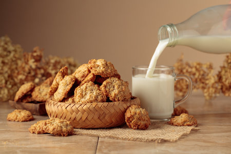 Oatmeal cookies and milk sit on a kitchen table. Milk is poured from a bottle into a glass mug. Beige background with copy space.の写真素材
