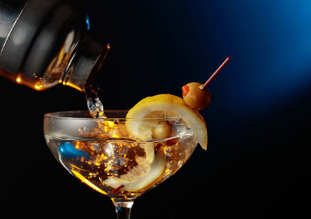 Martini with green olives and lemon. The cocktail is poured from a shaker into a glass.の写真素材