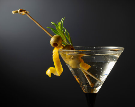 Classic dry martini cocktail with green olives, lemon peel, and rosemary on a black background. Free space for your text.の写真素材