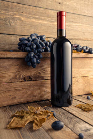 Bottle of red wine with grapes on an old wooden table.の写真素材