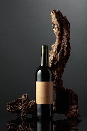 Bottle of red wine with old empty label. In the background old weathered snag. Black reflective background. Frontal view with space for your text.の写真素材