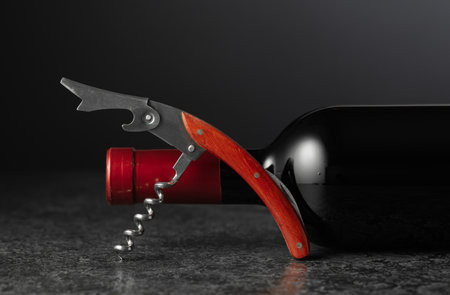Corkscrew and bottle of red wine on a black stone table. Copy space.の写真素材