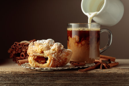 Strudel and coffee on an old wooden table. Fresh baked goods with anise and cinnamon, sprinkled with powdered sugar. Cream is poured into a coffee.の写真素材