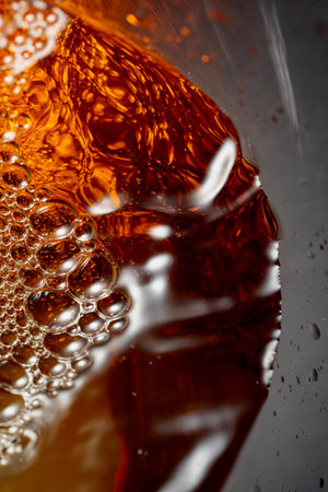 Golden drink is poured into the glass, creating beautiful waves and splashes. Selective focus. Macro shot.の写真素材