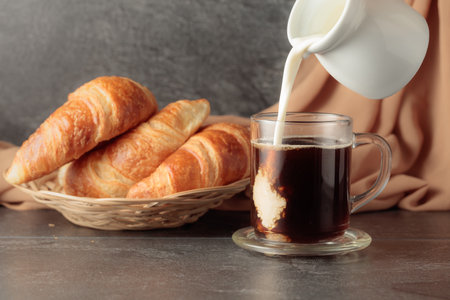 Freshly baked croissants and coffee with cream. Pouring creme in a glass cup of coffee.の写真素材