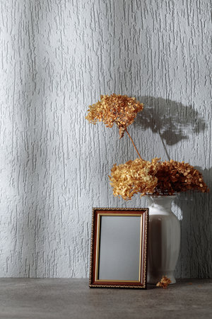 Empty picture frame and white vase with dry flowers on a background of gray wall. Wooden frame with golden ornament. Place your image in the frame. Copy space.の写真素材
