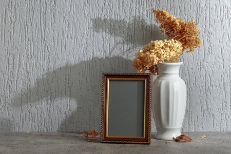 Empty picture frame and white vase with dry flowers on a background of gray wall. Wooden frame with golden ornament. Place your image in the frame. Copy space.の写真素材