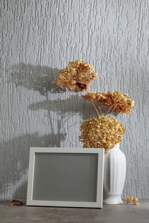 Empty picture frame and white vase with dry flowers on a background of gray wall. Place your image in the frame. Copy space.の写真素材