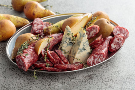 Blue cheese, dry-cured sausages, thyme and pears on a gray stone table.の写真素材