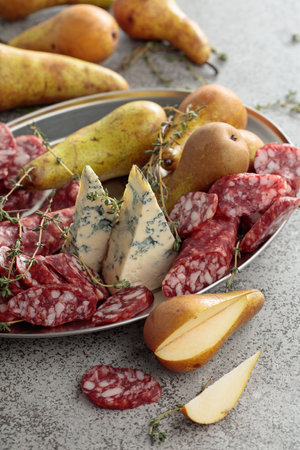 Blue cheese, dry-cured sausages, thyme and pears on a gray stone table.の写真素材