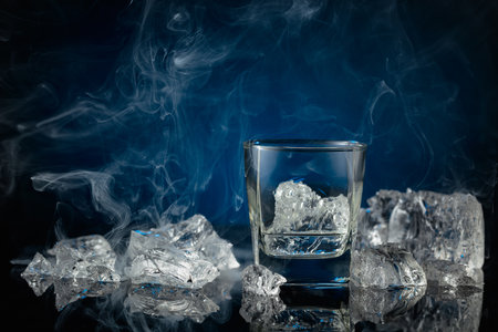 Crystal clear vodka or gin in a glass with ice. Vodka and ice pieces on a dark blue background. Copy space.の写真素材