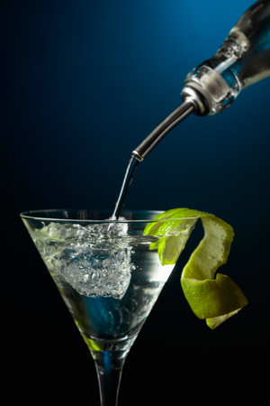 Vodka or gin is poured into a glass with ice. Cocktail garnished with lime peel.の写真素材