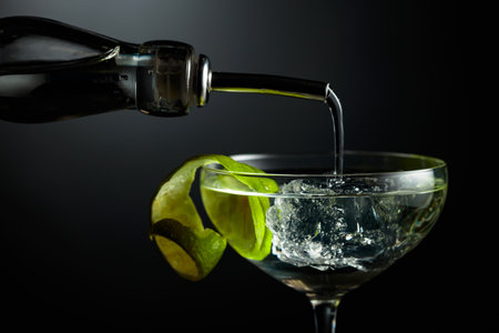 Vodka or gin is poured into a glass with ice. Cocktail with lime peel on a dark background.の写真素材