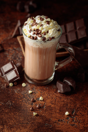 Hot chocolate cocoa drink with whipped cream. Cocoa drink in glass mug and pieces of bitter chocolate on a dark brown background.の写真素材