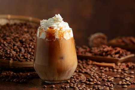 Iced caramel latte topped with whipped cream and caramel sauce. Refreshing and sweet coffee drink on a brown table.の写真素材