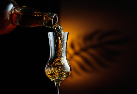 Strong alcoholic drink being poured from a bottle into a glass. Snifter on a black background. Copy space.の写真素材