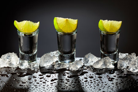 Tequila shots with lime slices on a wet black table. Strong alcoholic drink and crushed ice.の写真素材