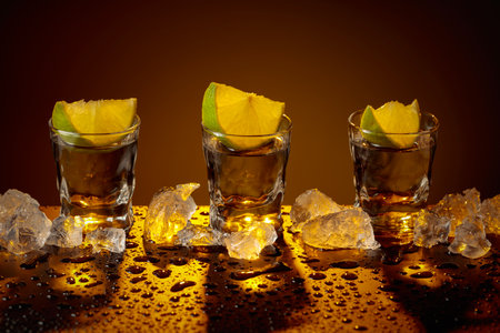 Tequila shots with lime slices on a wet black table. Strong alcoholic drink and crushed ice.の写真素材