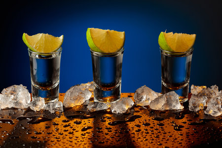 Tequila shots with lime slices on a wet black table. Crushed ice.の写真素材