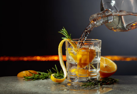 Refreshing gin-tonic cocktail with lemon and rosemary. Drink is poured from a bottle into a glass with ice. Copy space.の写真素材