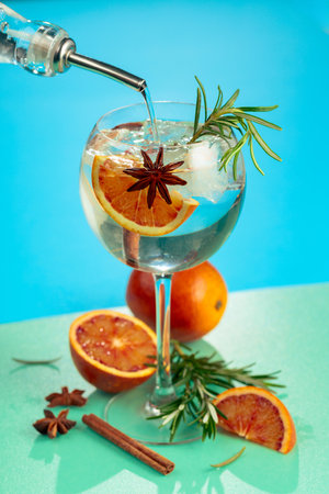 Summer cocktail with gin, tonic, blood orange, cinnamon, anise, and rosemary. Served on ice, bursting with color and freshness. Bright colorful background.の写真素材