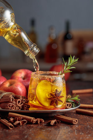 Apple cider is poured from a bottle into a glass with apple slices, anise, and a rosemary branch. The glass is garnished with sugar and cinnamon powder.の写真素材