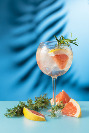 Cocktail gin and tonic with ice and grapefruit slices. Blue background with shadow of palm leaf. Copy space.の写真素材