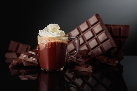 Hot chocolate with whipped cream. On a background bitter broken chocolate bar. Black reflective background with copy space.の写真素材