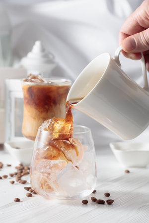 Black coffee is poured into a glass with iced. Chilled coffee with natural ice on a white wooden table.の写真素材