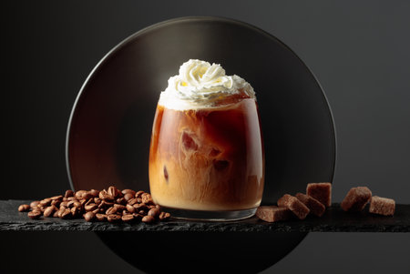 Iced coffee with whipped cream and caramel sauce on a black background. Iced drink with coffee beans and brown sugar.の写真素材