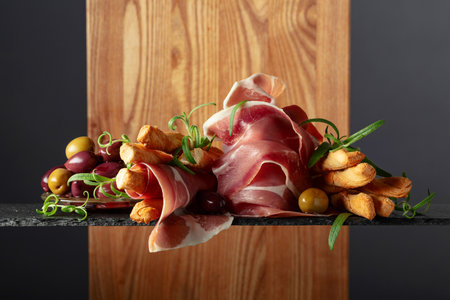 Prosciutto with bread sticks, olives, and rosemary on a black background. Traditional Italian snacks.の写真素材
