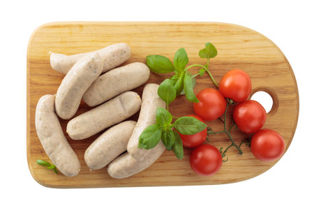 Traditional Bavarian white sausages with basil and tomatoes on a wooden cutting board. Isolated on a white background. Top view.の写真素材