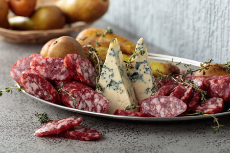 Blue cheese, dry-cured sausages, thyme and pears on a gray stone table.の写真素材