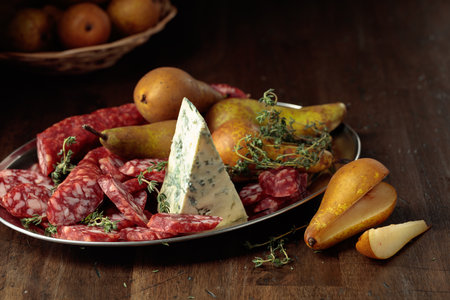 Dry-cured sausages, blue cheese, thyme and pears on a wooden table. Simple healthy food. Copy space.の写真素材