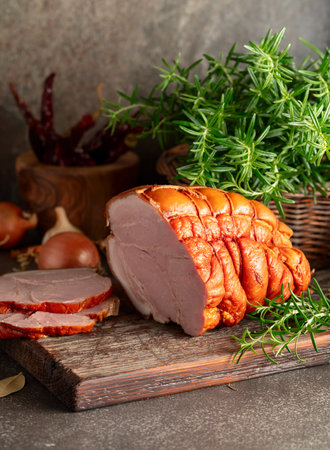 Tasty smoked pork ham with rosemary, onion, garlic, red pepper, and bay leaves. Smoked meat on a kitchen table.の写真素材