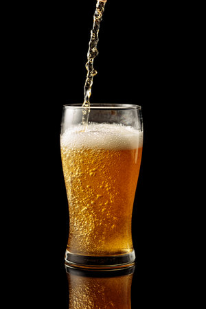 Pouring beer into a glass. Glass of beer on a black reflective background.の写真素材