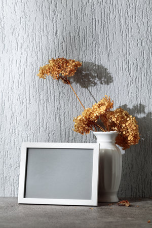 Empty picture frame and white vase with dry flowers on a background of gray wall. Place your image in the frame. Copy space.の写真素材