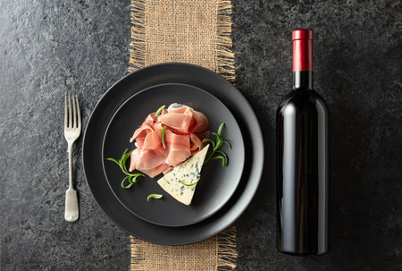 Bottle of red wine with blue cheese, prosciutto, and rosemary on a blackstone table. Top view. Copy space.の写真素材