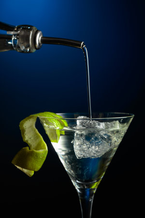 Vodka or gin is poured into a glass with ice. Cocktail garnished with lime peel.の写真素材