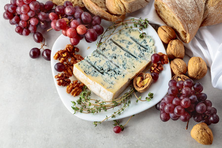Gorgonzola cheese with walnuts, red grapes, and thyme on a white kitchen table.の写真素材