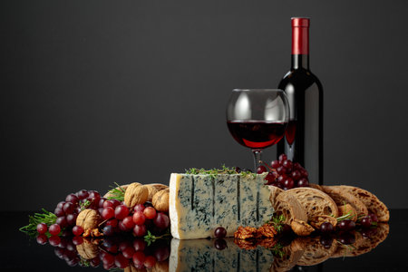 Gorgonzola cheese with ciabatta, walnuts, grapes, and red wine. Tradition Italian blue mold cheese with fruits and aromatic herbs on a black reflective background.の写真素材