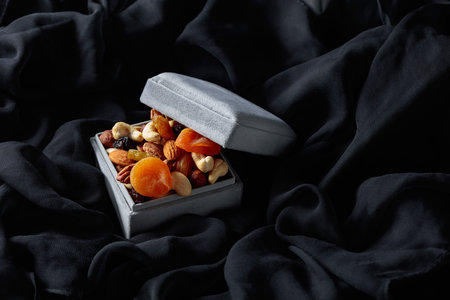 Dried fruits and nuts in a gift box on a black cloth.の写真素材