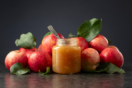 Jar of apple jam and red fresh apples with leaves on a black background.の写真素材