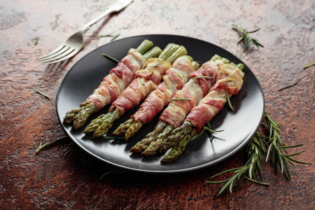 Grilled green asparagus with bacon in black plate on a brown vintage background.の写真素材